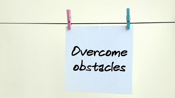 Overcome obstacles. Note is written on a white sticker that hangs with a clothespin on a rope on a background of beige wall